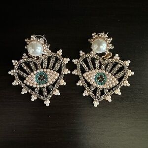 A pair of evil eye studded earrings with heart and pearl accent stud post.